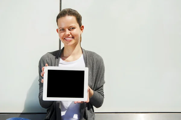 Mujer sosteniendo una tableta sobre una pared de vidrio sonriendo — Foto de Stock