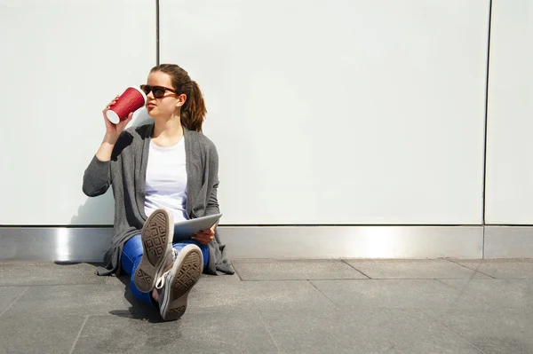 Ung tonåring dricker kaffe och tittar åt sidan med tablett — Stockfoto