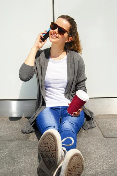 Junges glückliches Teenie-Mädchen mit einem Smartphone über die Wand im Rücken — Stockfoto