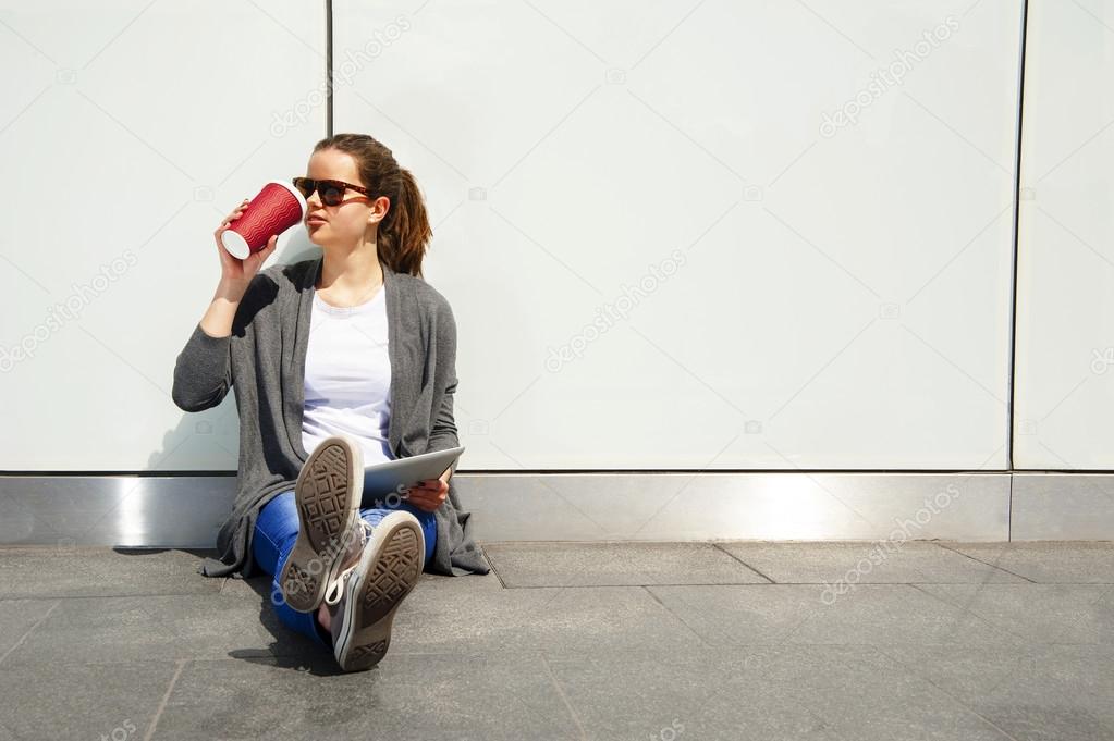 Young teenager drinking coffe and looking aside with tablet
