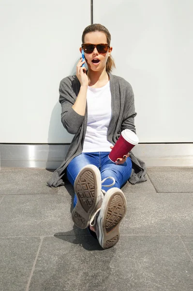 Junge Frau lehnt sich schockiert an Wand und telefoniert mit Sonnenbrille — Stockfoto
