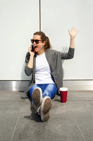 Junges glückliches Teenie-Mädchen mit einem Smartphone über die Wand im Rücken — Stockfoto