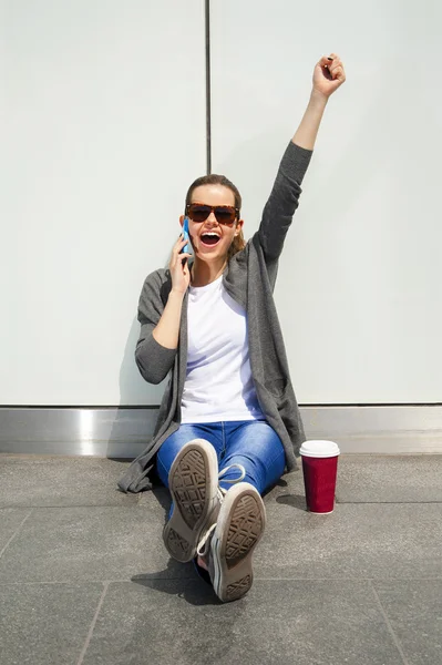 Junges glückliches Teenie-Mädchen mit einem Smartphone über die Wand im Rücken — Stockfoto