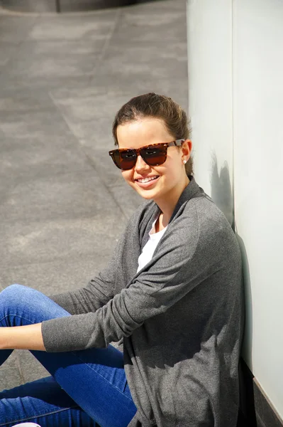 Hermosa mujer joven de moda sentarse en la calle junto a la pared con —  Fotos de Stock