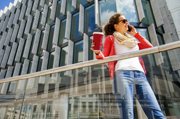 Mujer bastante joven usando teléfono móvil sosteniendo taza de café Imágenes de stock libres de derechos