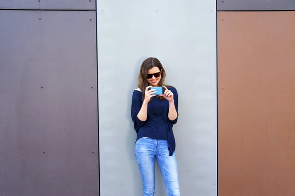 Una mujer tomando fotos con un celular junto a la pared. Chica feliz en cit — Foto de Stock