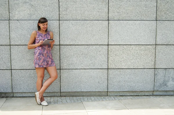 Mujer joven usando la tableta de pie contra la pared en la ciudad s — Foto de Stock