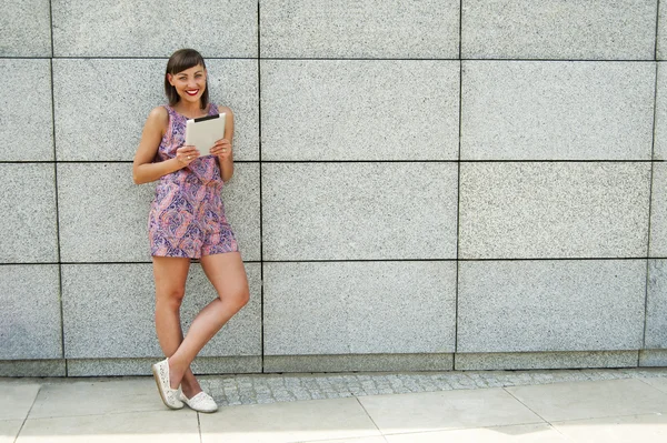 Mujer joven usando la tableta de pie contra la pared en la ciudad s —  Fotos de Stock