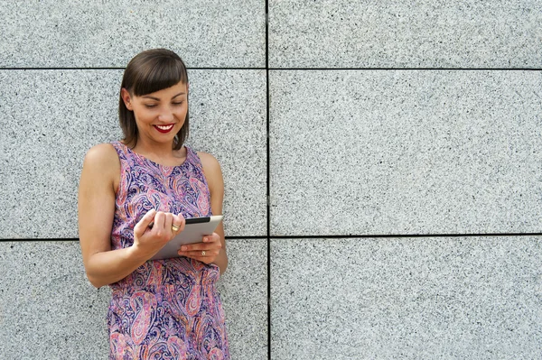 Mujer joven usando la tableta de pie contra la pared en la ciudad s — Foto de Stock