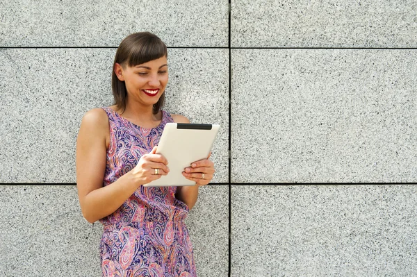 Ung kvinna använder tablet stående mot väggen i staden s — Stockfoto