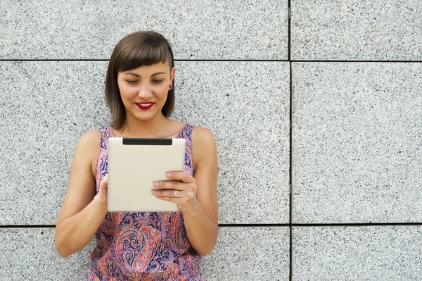 Jovem mulher moderna usando tablet na cidade pela parede, sorrindo — Fotografia de Stock