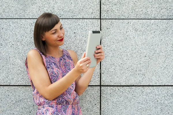 Jovem mulher usando tablet de pé contra a parede na cidade s — Fotografia de Stock