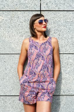 Duvarın içinde şehir gülümseyen güneş gözlüklü genç modern kadın.