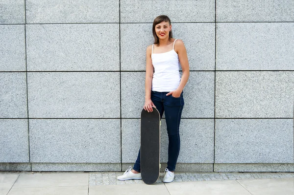 Chica joven con monopatín en la ciudad por la pared sonriendo . —  Fotos de Stock