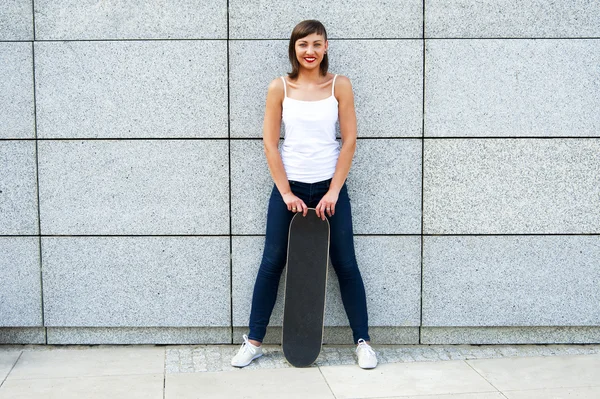 Jong meisje met skateboard in de stad door de muur glimlachende. — Stockfoto