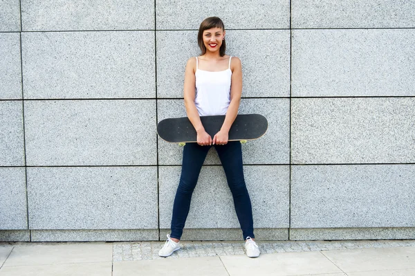 Νεαρό κορίτσι με skateboard στην πόλη από το τοίχο χαμογελά. — Φωτογραφία Αρχείου