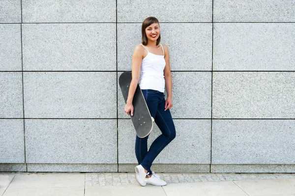 Jong meisje met skateboard in de stad door de muur glimlachende. — Stockfoto