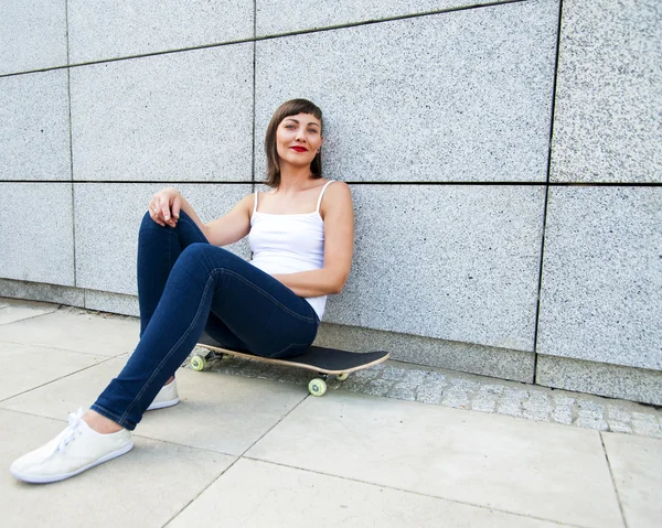 Junges modernes Mädchen sitzt auf Skateboard an der Wand in der Stadt. — Stockfoto