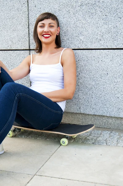 Μοντέρνα κοπέλα καθίσει για skateboard από τον τοίχο στην πόλη. — Φωτογραφία Αρχείου