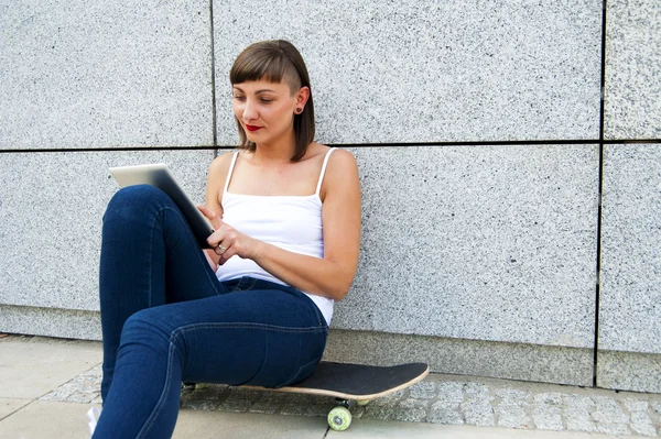 Young girl siting on skateboard in the cty with tablet by the wa — Stock Photo, Image