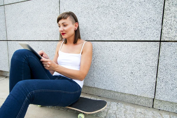 Young girl siting on skateboard in the cty with tablet by the wa — Stock Photo, Image