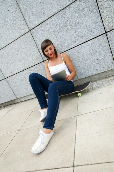 Giovane ragazza seduta su skateboard nel cty con tablet dal wa — Foto Stock