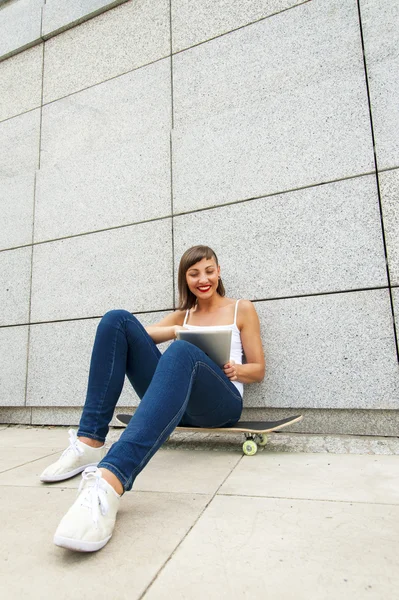Young girl siting on skateboard in the city with tablet by the w — Stock Photo, Image