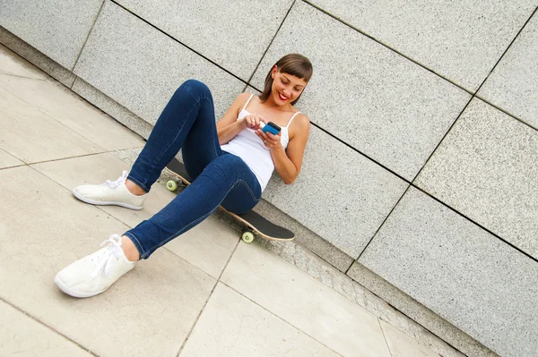 Jong meisje aanbrengen op skateboard in de stad met telefoon door de wa — Stockfoto