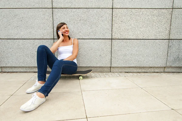 Young girl siting on skateboard in the city talking by phone nea — Stock Photo, Image