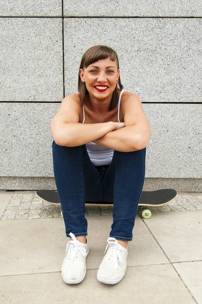 Moderne meisje zitten op skateboard door de muur in de stad. — Stockfoto