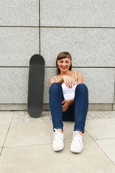 Mladá dívka s skateboard ke zdi v městě, s úsměvem. — Stock fotografie