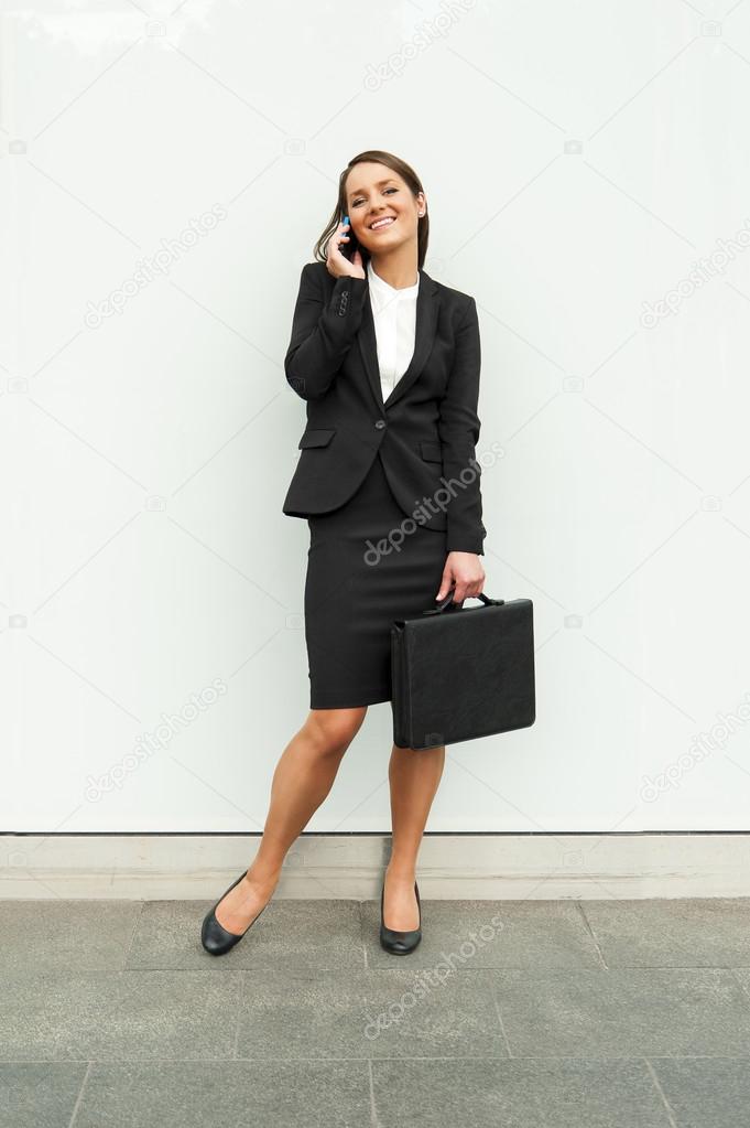 Business woman standing by the white glass wall in the city with