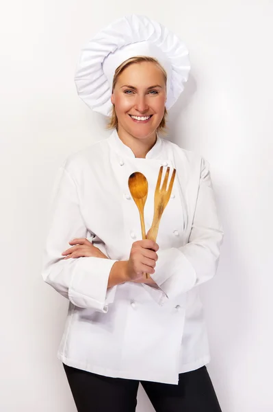 Young woman chef holding wooden spoon and fork, smiling. — Stock Photo, Image