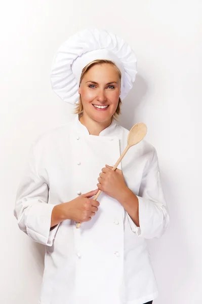 Mujer chef en traje de cocinero sosteniendo cuchara de madera y sonriendo a ca — Foto de Stock