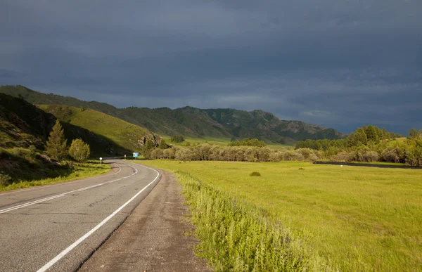 Mountain road in the rays of the setting sun — Stock Photo, Image