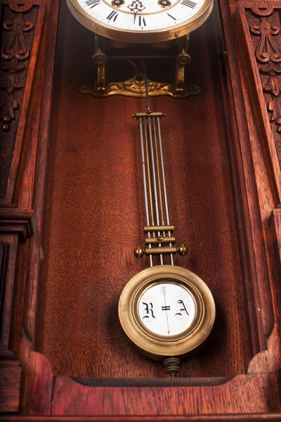 Antique wall clock with a pendulum in a carved wooden housing.