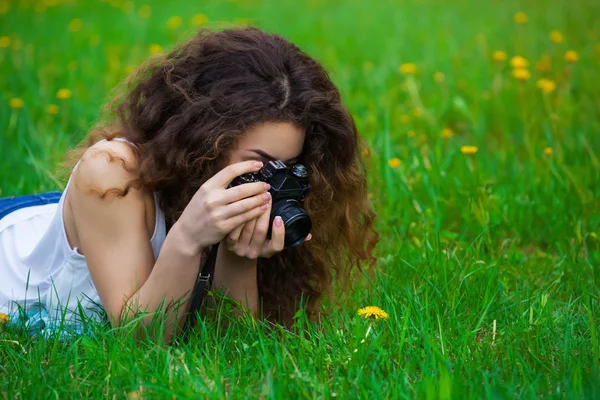 Piękne dziewczyny fotograf z kręconymi włosami, leżąc na trawie i — Zdjęcie stockowe