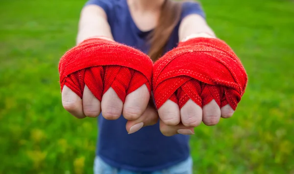 Meisje atleet, bokser permanent in het park en het strekt beide handen in vuisten gebalde verpakt sport, rode bandages boksen vooruit. Voorbereiding op de opleiding. Het concept van sport en een gezonde levensstijl. — Stockfoto