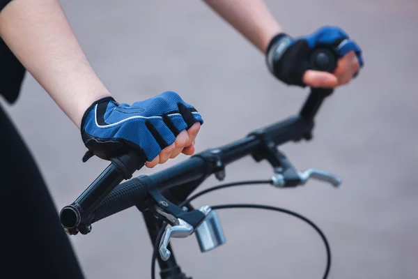 Hands of a girl in a sports blue-black gloves holding on to the steering wheel of the bicycle. Close-up. — Stock Photo, Image