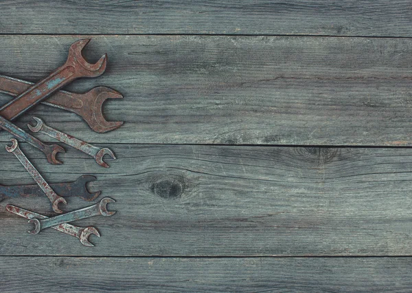 In the old, wooden, cracked, the working surface in the workshop lie in the left corner of the vintage, used, rusty, discolored, steel, metal, dirty wrenches of different sizes. — Stock Photo, Image