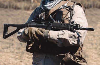 Bir asker bir saldırı tüfeği tutan bir yelek giyiyor.