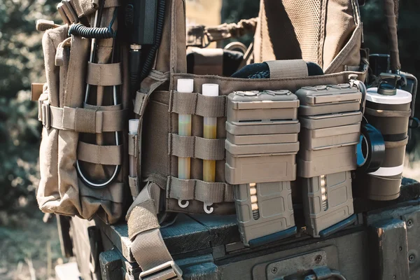 Chaleco del ejército con un walkie-talkie, collares cargados, granadas aturdidoras, palos luminosos, de pie en una caja de madera de munición . — Foto de Stock