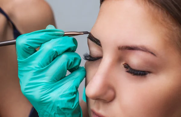 Kosmetolog- makeup artist applies paint henna on previously plucked, design, trimmed eyebrows in a beauty salon in the session correction. Professional care for face. — Stock Photo, Image