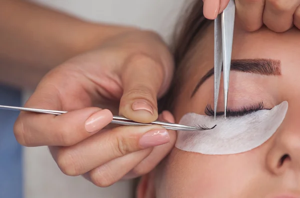 Il Maestro di trucco corregge, e rafforza raggi di ciglia, tirando fuori un paio di pinzette in un salone di bellezza. Cura professionale della pelle e degli occhi. — Foto Stock