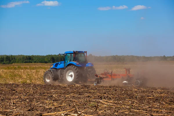 Grote blauwe trekker plows van het gebied en verwijdert de overblijfselen van prev — Stockfoto