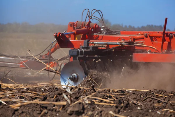 Grote trekker trekken een ploeg en de ploeg het veld verwijderen de overblijfselen van de eerder schuine zonnebloem. Het werk van landbouwmachines. — Stockfoto