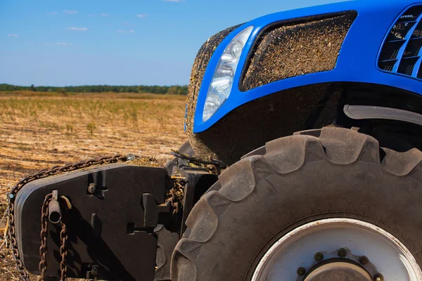 Het voorste deel van een blauwe trekker close-up. Landbouw machine staande in een veld tijdens het ploegen en oogsten van de bodem. — Stockfoto