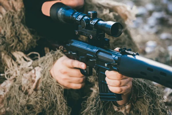 El soldado disfrazado en un pasamontañas y camuflaje militar tiene como objetivo en la mira de un fusil de francotirador. Zona de guerra. — Foto de Stock