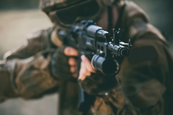 El soldado en el desempeño de tareas en camuflaje, guantes, casco y lentes tintados sosteniendo una ametralladora tiene como objetivo de tiro. Zona de guerra. — Foto de Stock