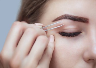 Makyöz, güzellik salonundaki genç bir kadının kaşlarını alıyor. Profesyonel cilt bakımı ve makyaj.